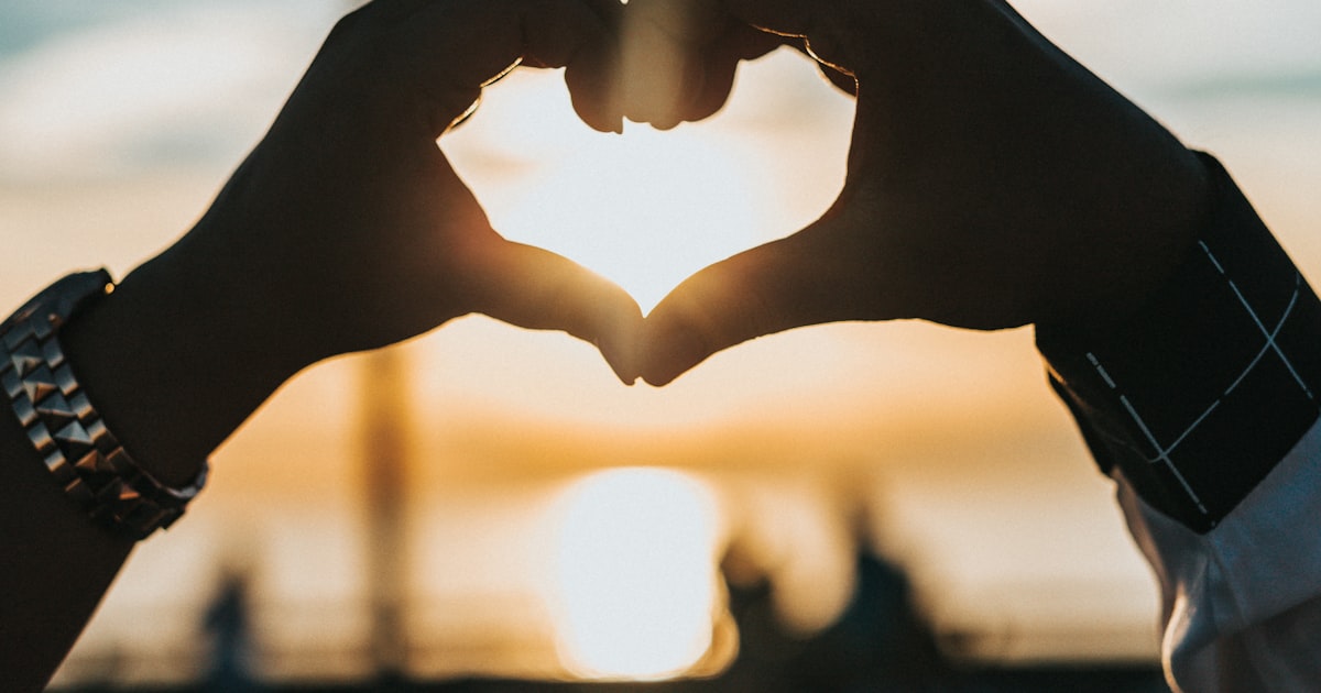 Hands forming a heart shape against a soft sunset light, representing calm reassurance about perimenopause heart palpitations